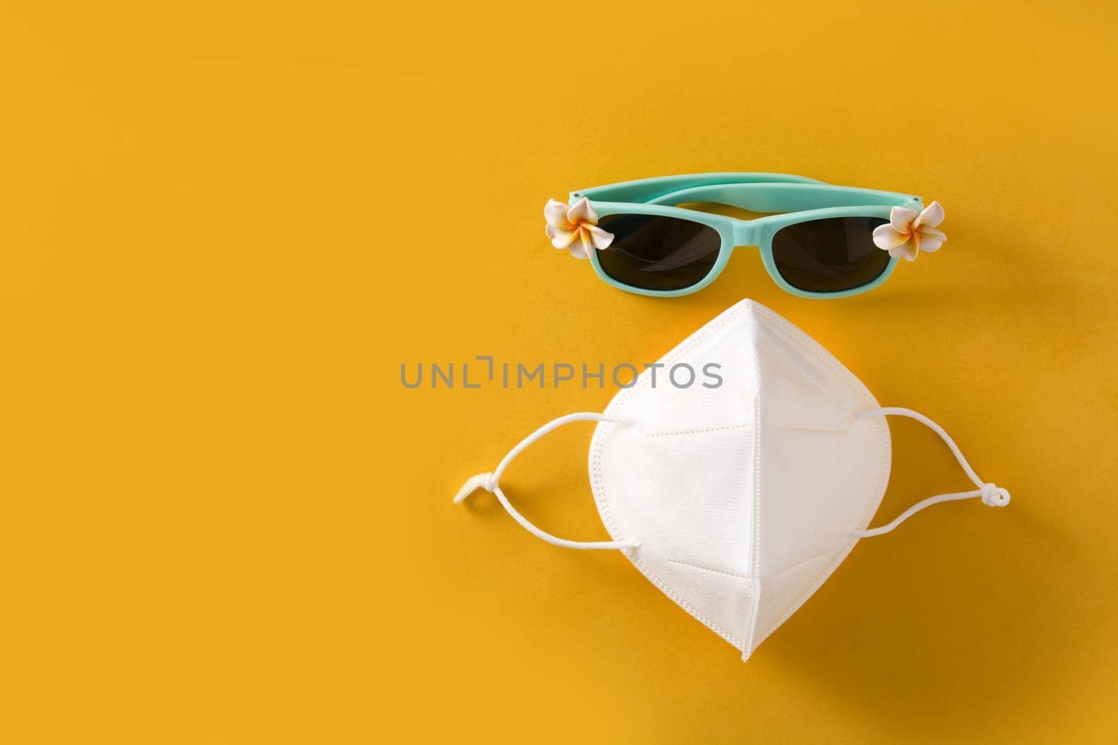 Sunglasses and protective face mask on yellow background. COVID-19 summer concept.