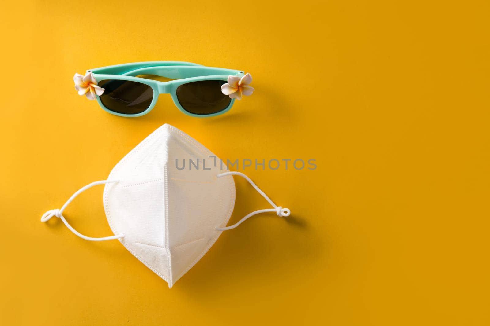 Sunglasses and protective face mask on yellow background. COVID-19 summer concept.