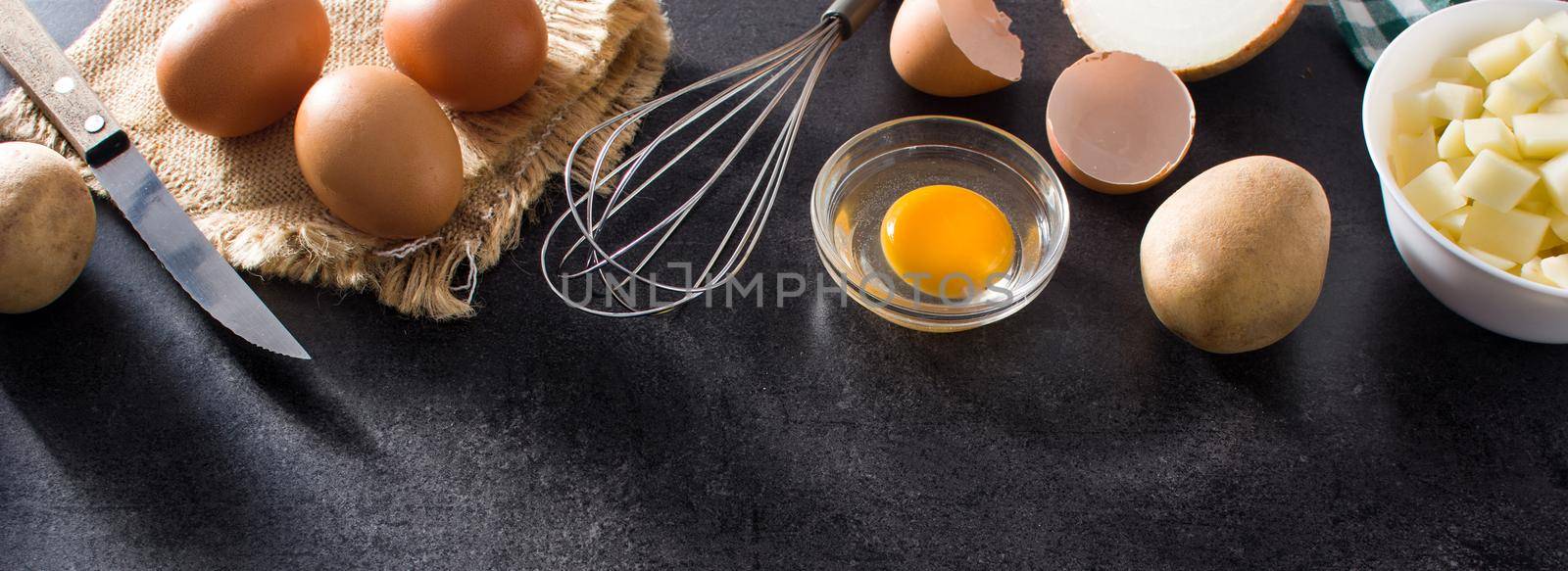 Spanish omelette tortilla ingredients: eggs, potatoes and onion on black slate background. Top view copy space