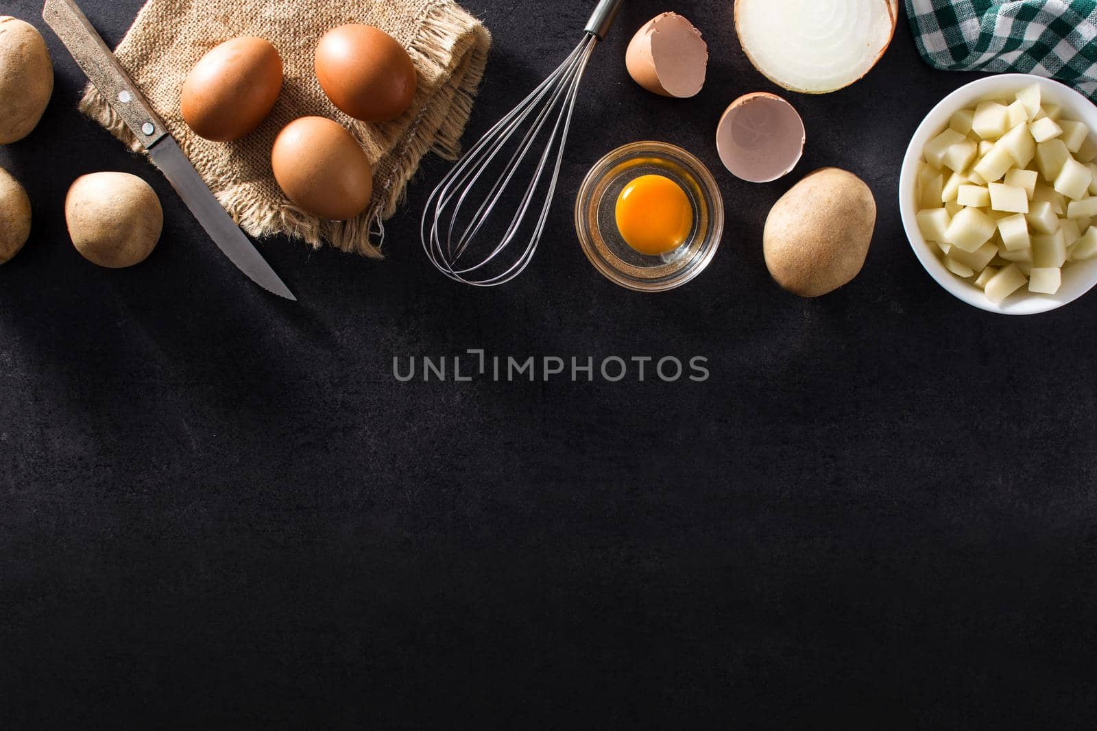 Spanish omelette tortilla ingredients: eggs, potatoes and onion on black slate background