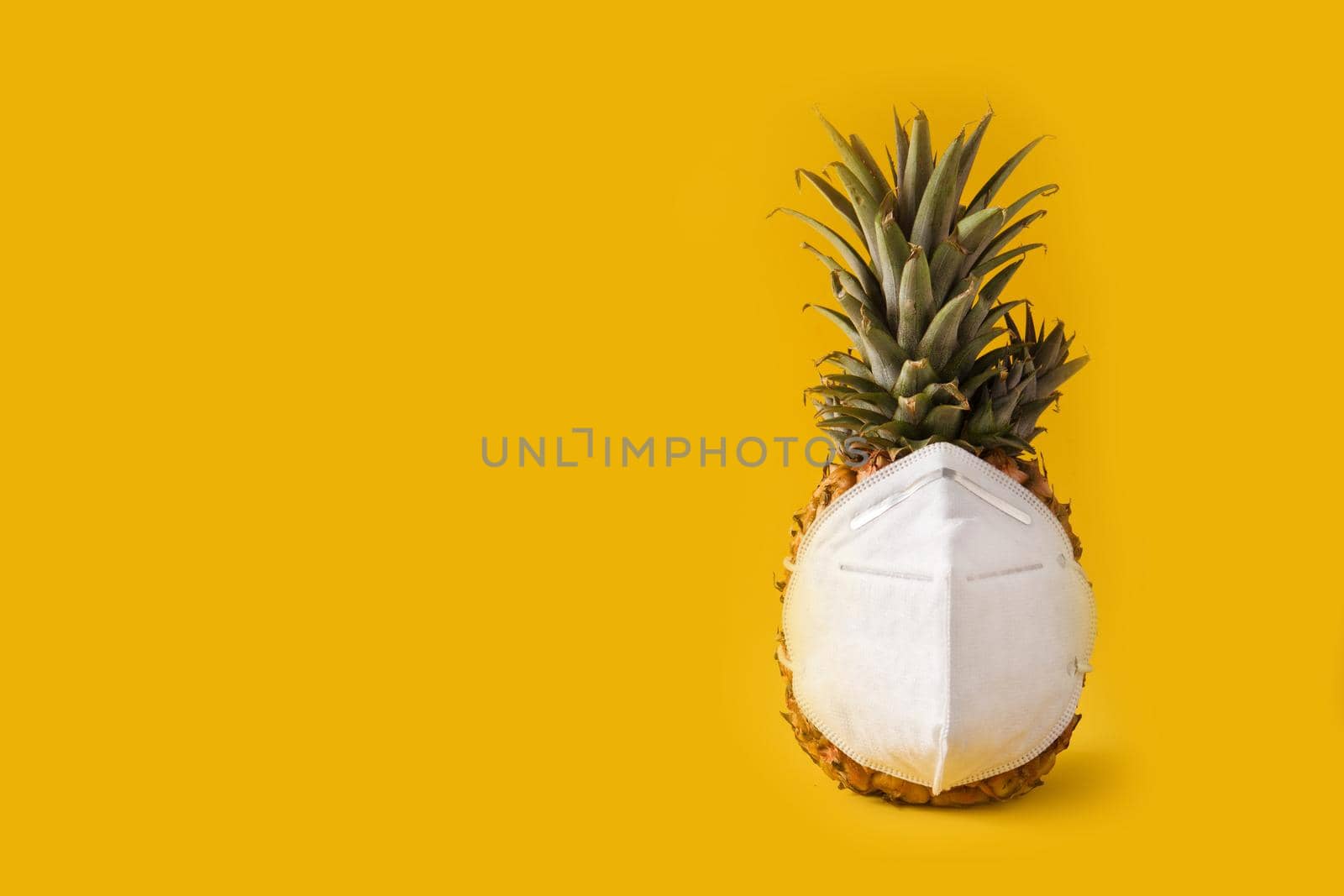 Pineapple with protective face mask on yellow background. Summer COVID-19 concept