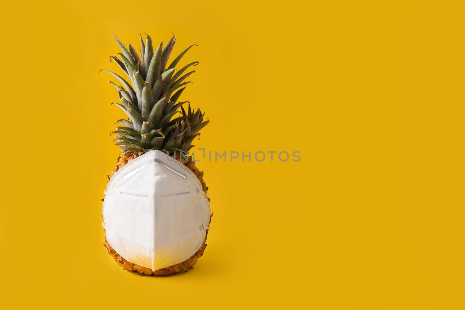 Pineapple with protective face mask on yellow background. Summer COVID-19 concept