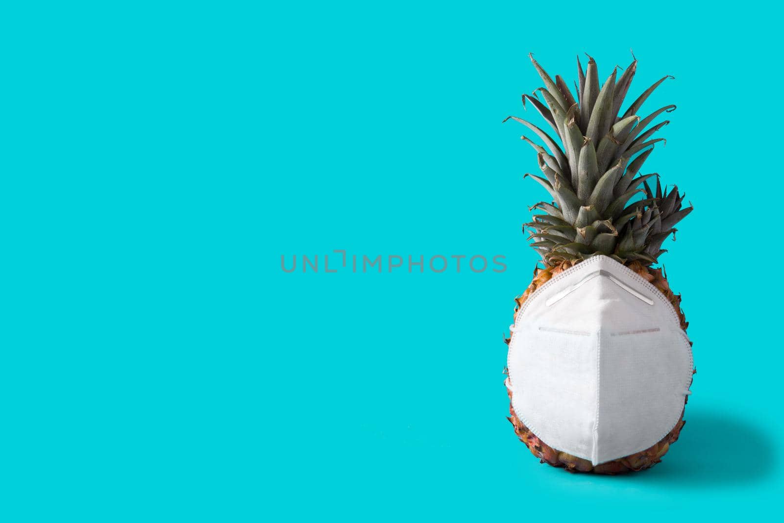 Pineapple with protective face mask on blue background