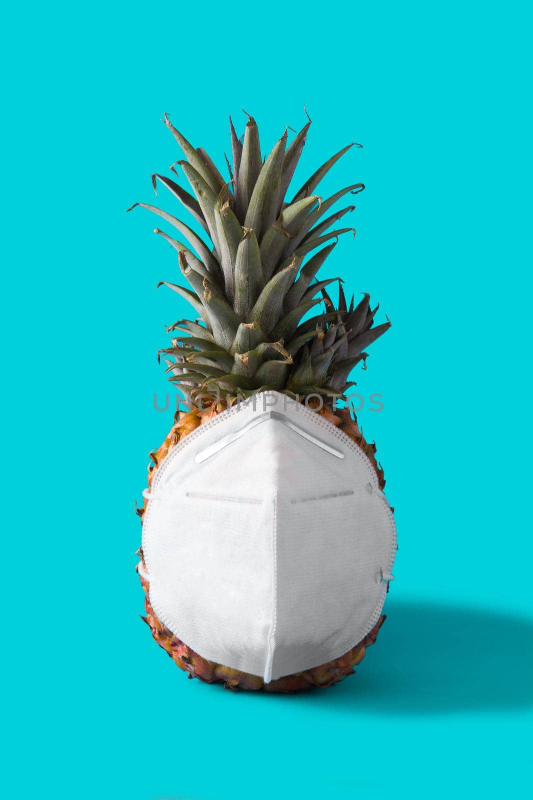 Pineapple with protective face mask on blue background