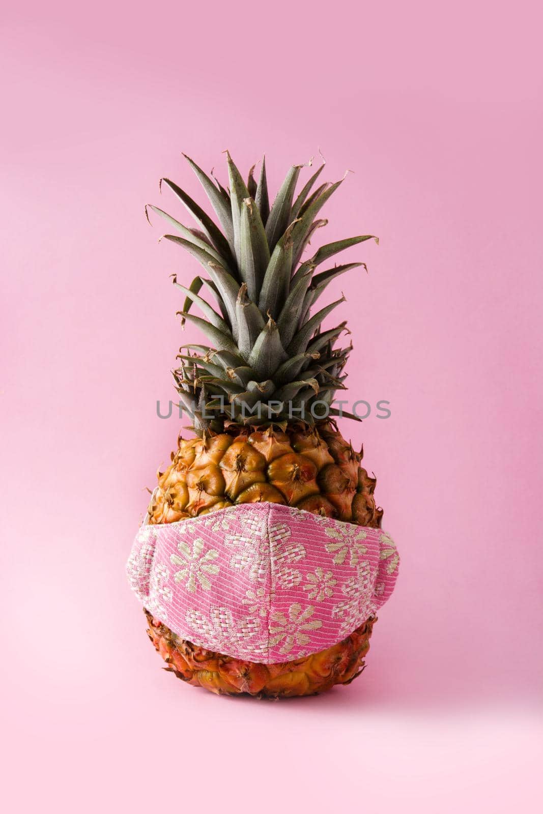 Pineapple with protective face mask on pink background