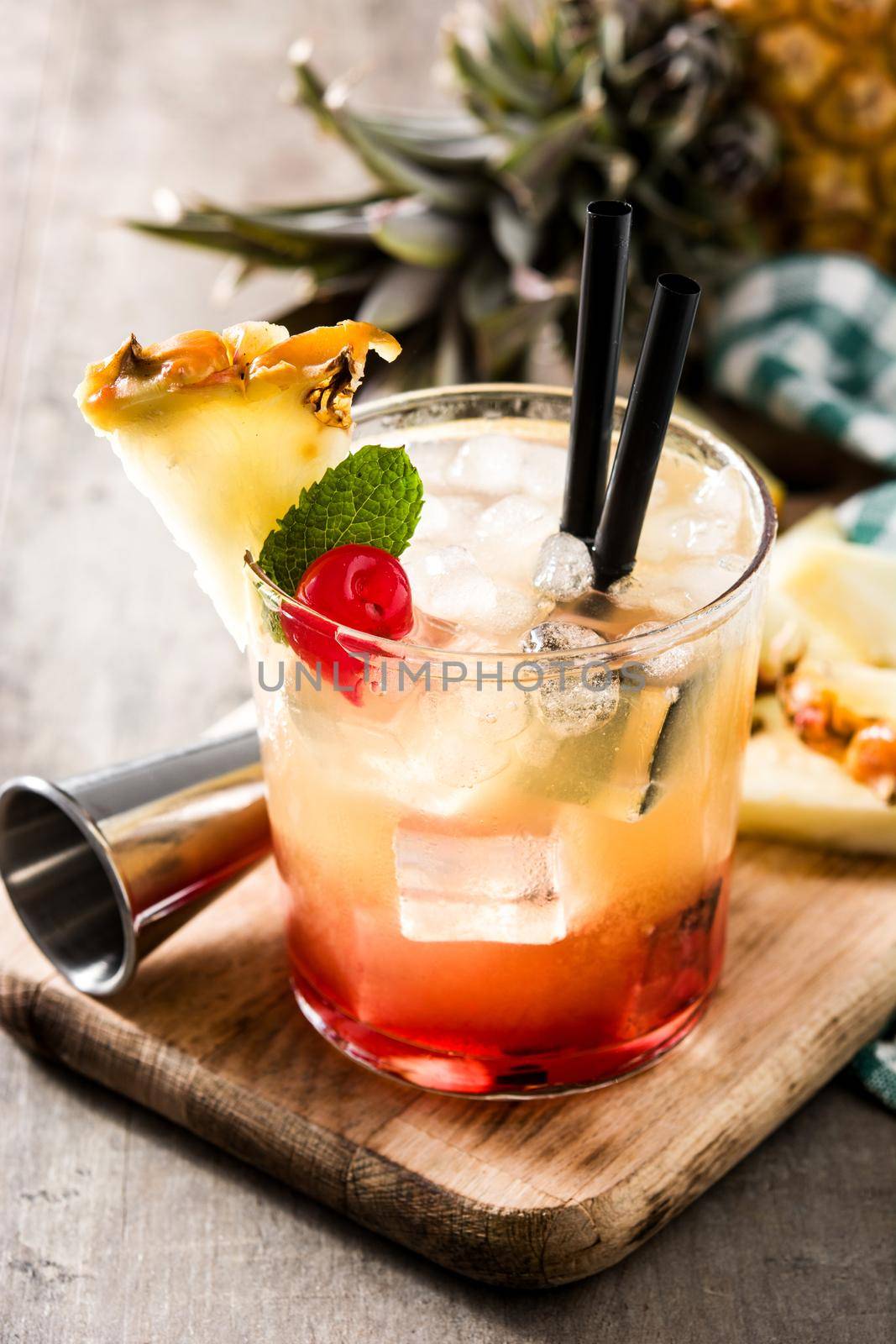 Cold mai tai cocktail with pineapple and cherry on wooden table