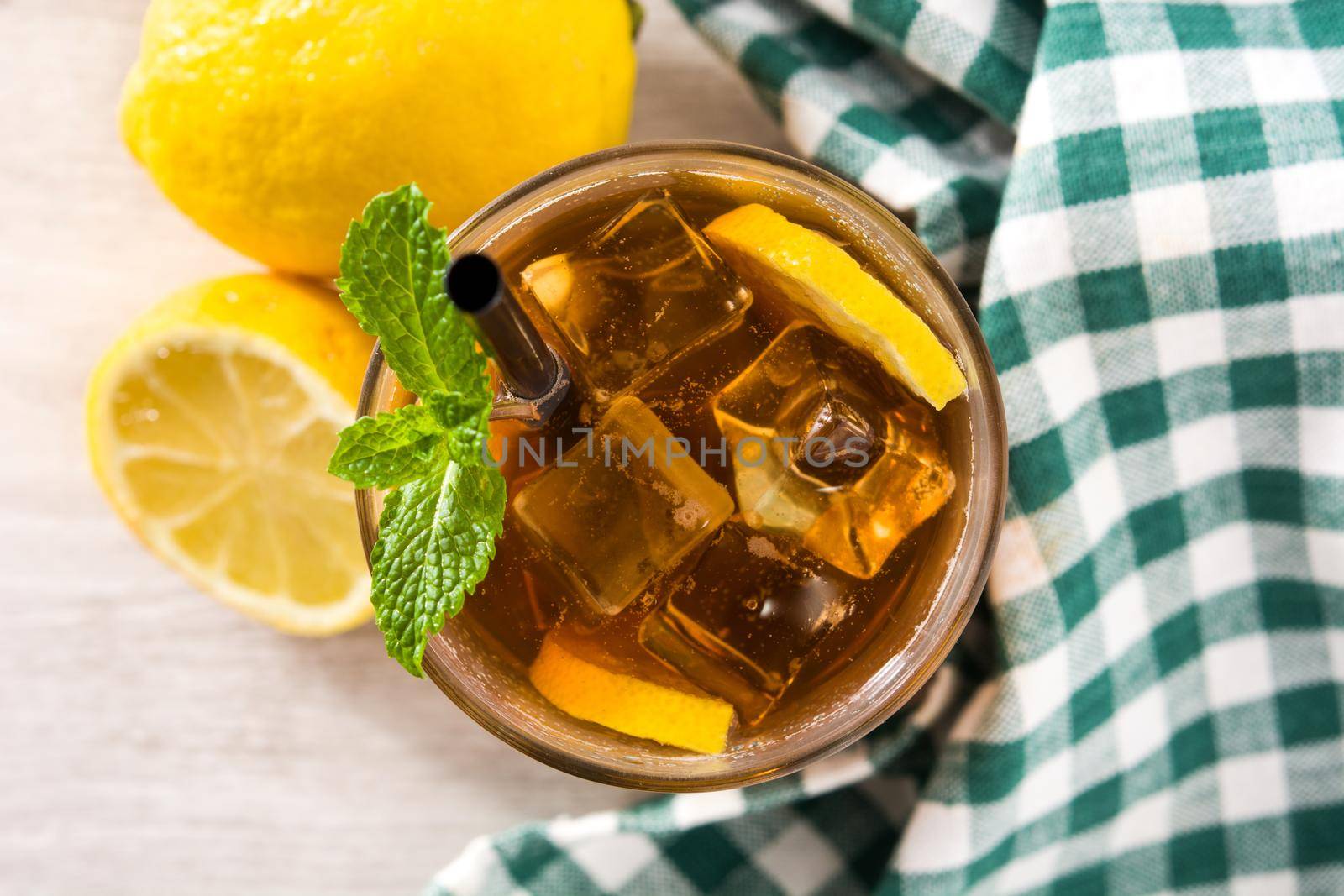 Iced tea drink with lemon in glass and ice on white wooden table