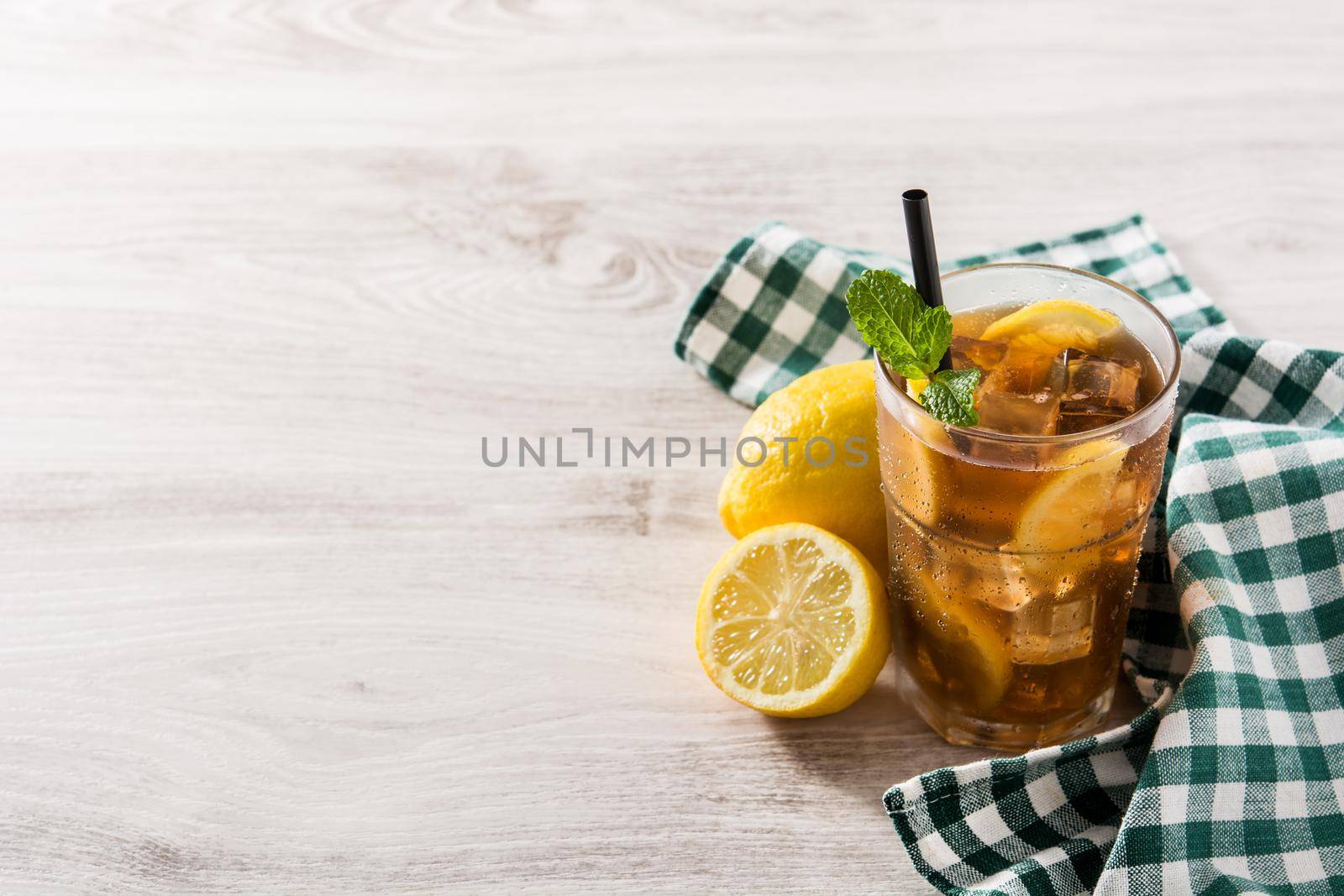 Iced tea drink with lemon in glass and ice on white wooden table