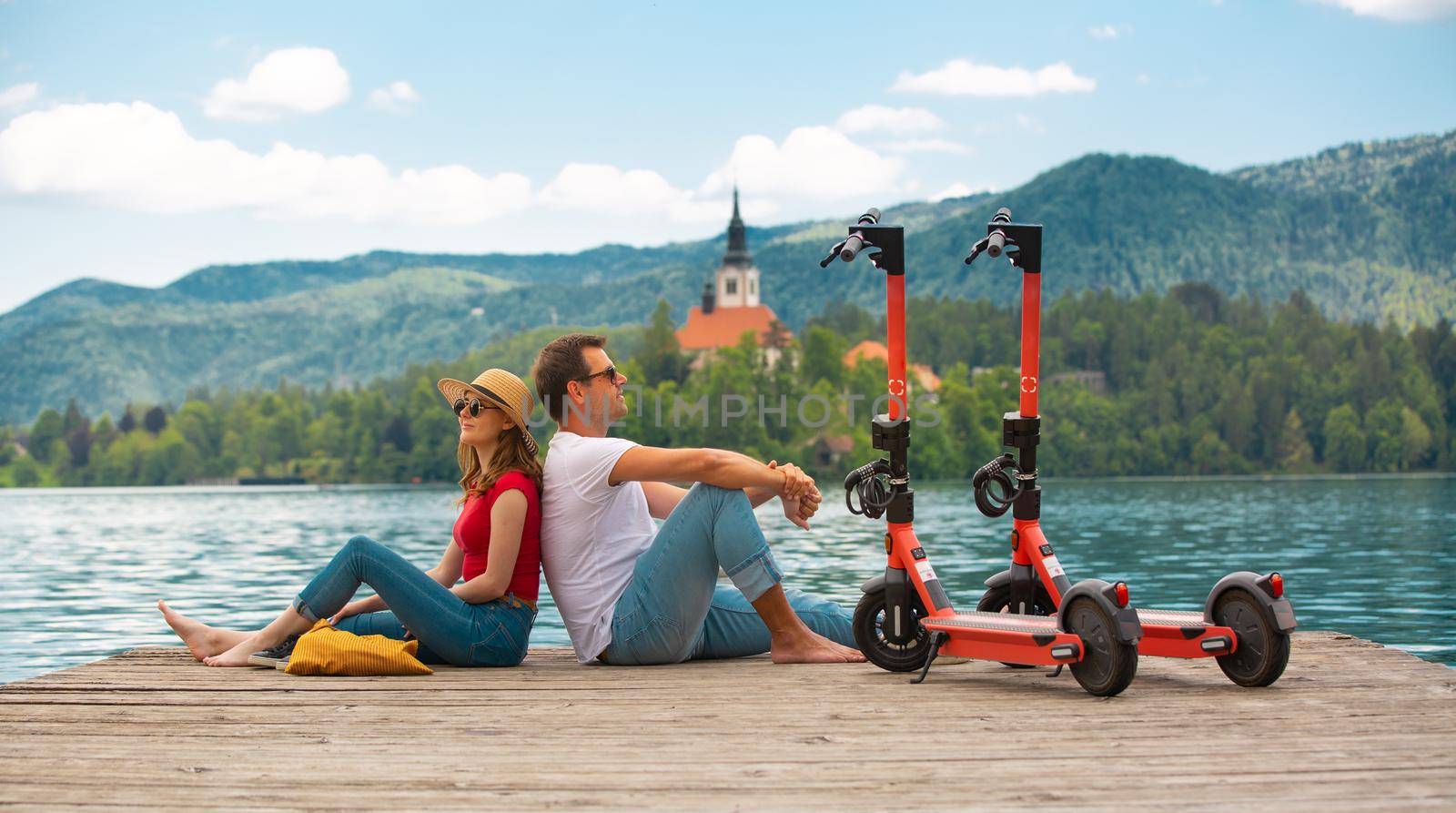 Young couple using electric scooter as modern ecological mean of transport while exploring green country Slovenia at vacations. Green eco energy concept with zero emission. Warm sunshine filter. by kasto