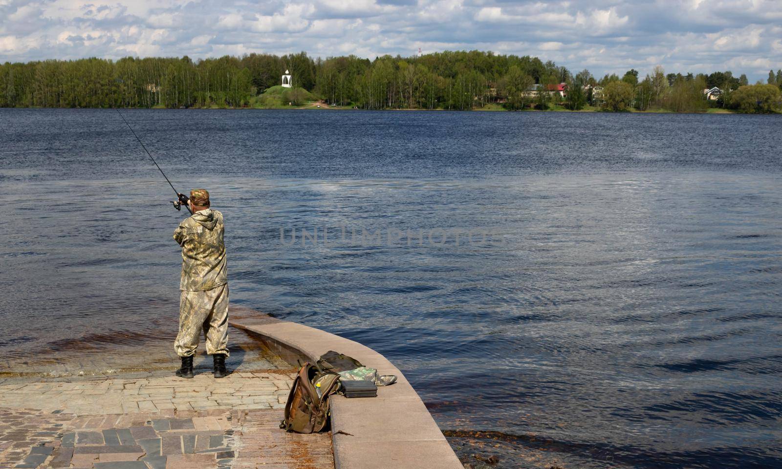 A fisherman in camouflage catches fish in the spring river.
