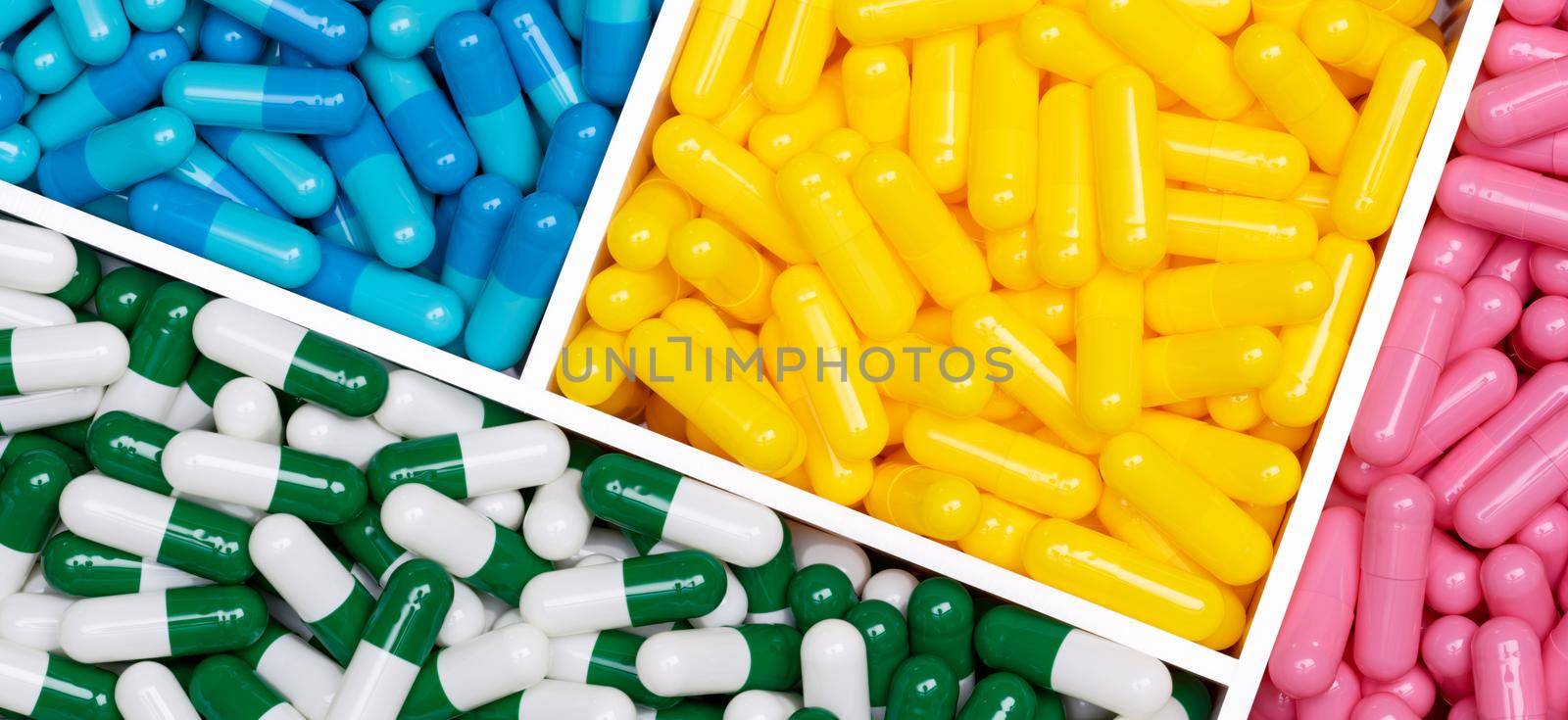 Top view of colorful capsule pills in plastic box. Pink, yellow, blue, green-white capsule pills in tray. Pharmacy web banner. Pharmaceutical industry. Healthcare background. Online pharmacy concept. by Fahroni