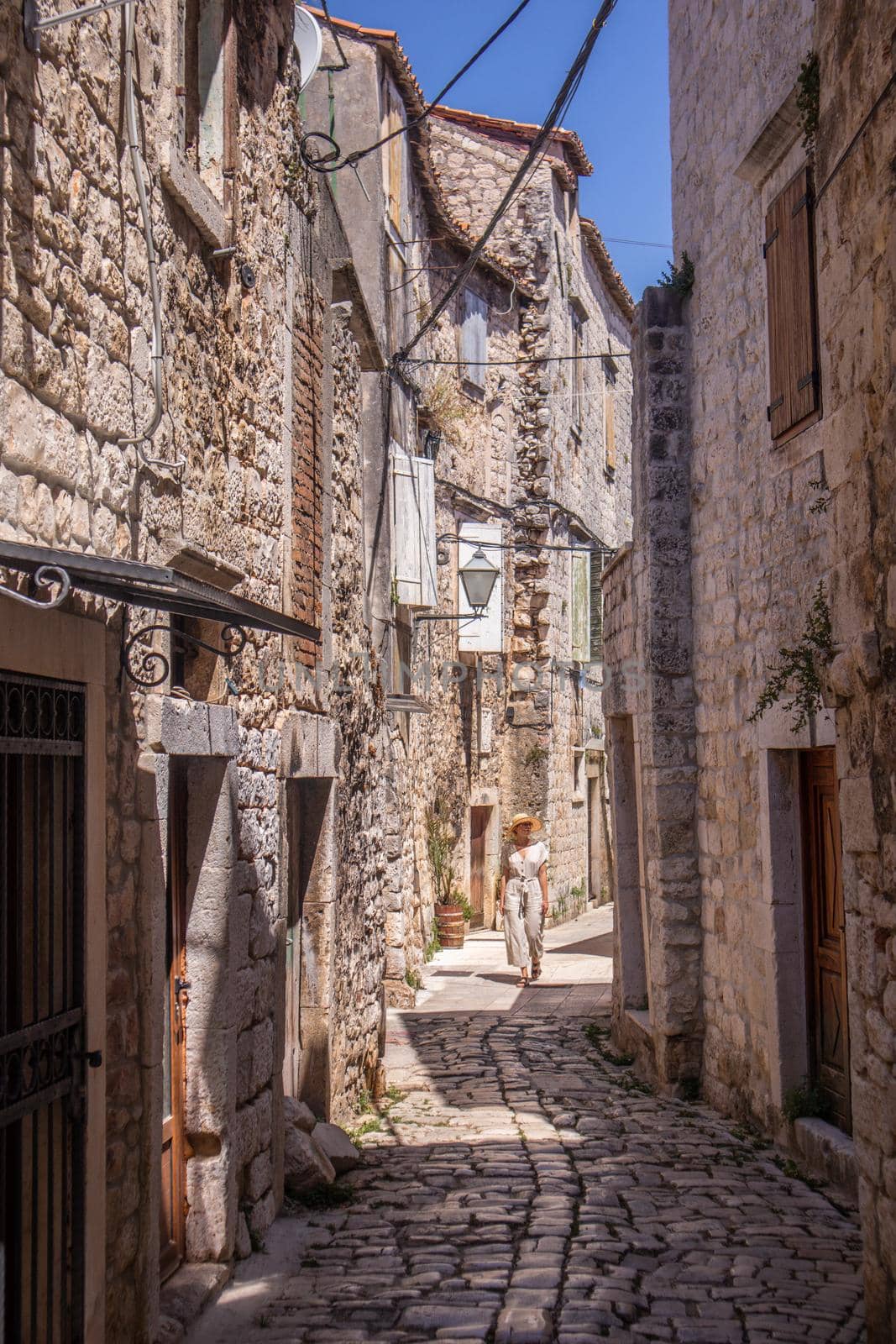 Beautiful blonde young female traveler wearing straw sun hat sightseeing and enjoying summer vacation in an old traditional costal town at Adriatic cost, Croatia.