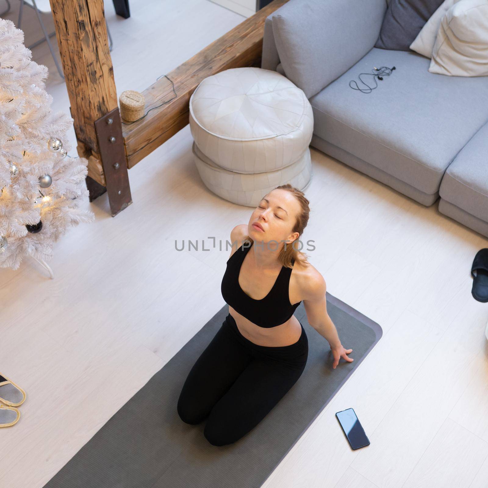 Beautiful blonde woman doing home workout indoors. Woman practice yoga at home. Fit girl using workout tutorials for healthy active lifestyle. Woman using quarantine for home workouts and stretching