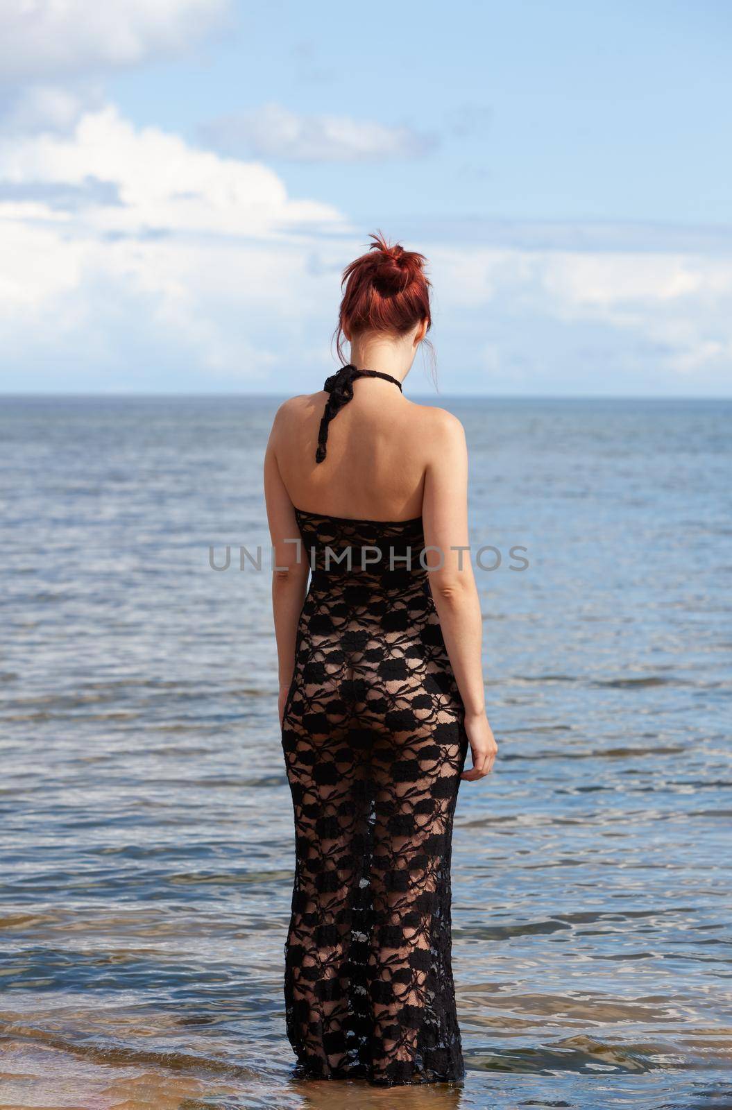 Young red-haired woman in a black lace dress on a naked body posing on the seashore