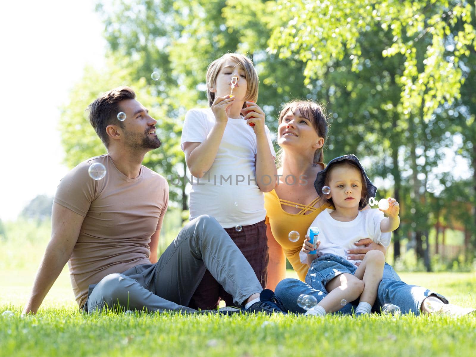 Happy family of parents and children outdoor playing with soap bubbles in park