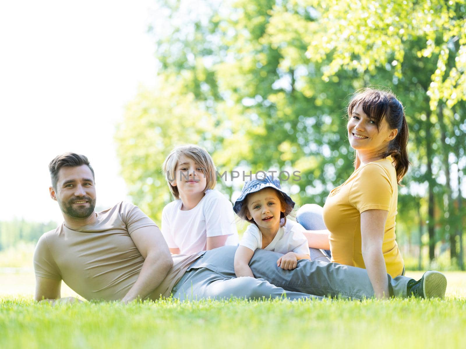 Portrait of happy family of parents and two children sitting in park outdoors and smiling