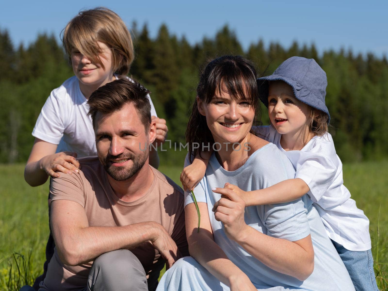 Portrait of happy family of parents and two children sitting on summer meadow outdoors and smiling