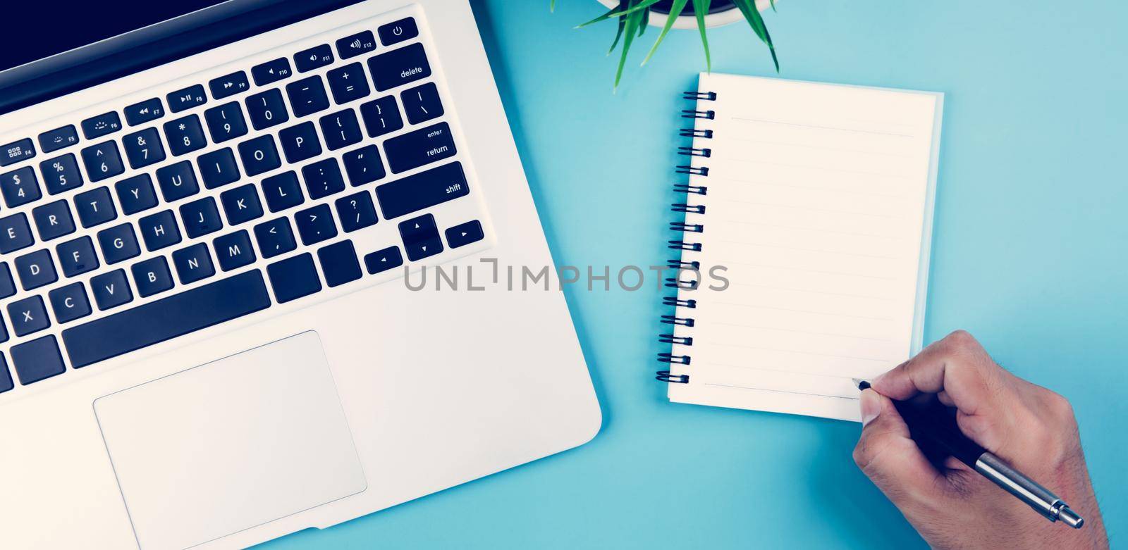 Flat lay, hand of businessman writing on notebook with Laptop computer and plant and pen on desk in office, workplace and notebook and potted tree and book, top view, business concept. by nnudoo