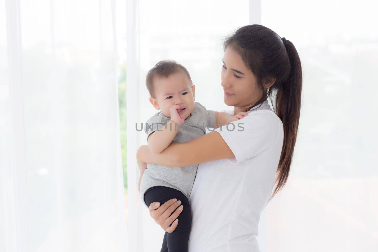 Young asian mother holding little baby girl and walking together in the bedroom at home, mom carry daughter and care, relationship of parent and child, toddler and parent, indoor, family concept. by nnudoo
