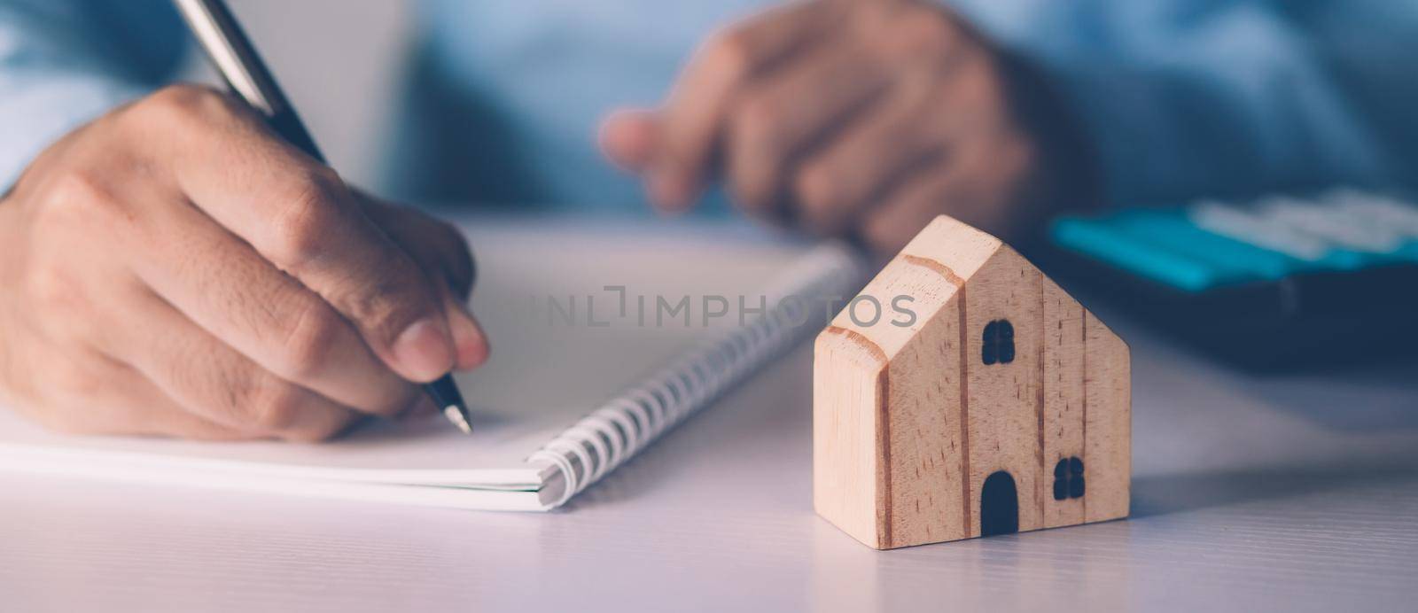 Hand of businessman planning and writing on note expense and mortgage with home, insurance house, finance and investment, calculate loan of residential, cost for refinance of property concept. by nnudoo