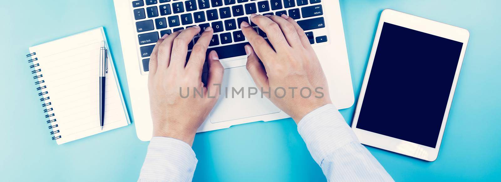 Hand of businessman working on laptop computer with tablet and notebook on desk in office, hand typing keyboard with book and pen, workplace with copy space, top view, flat lay, business concept. by nnudoo