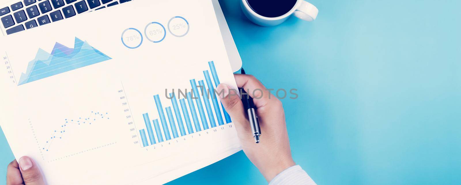 Hand of businessman holding documents report statistic financial with graph and chart and laptop computer and coffee on desk, finance and invest, digital marketing, business and communication concept. by nnudoo