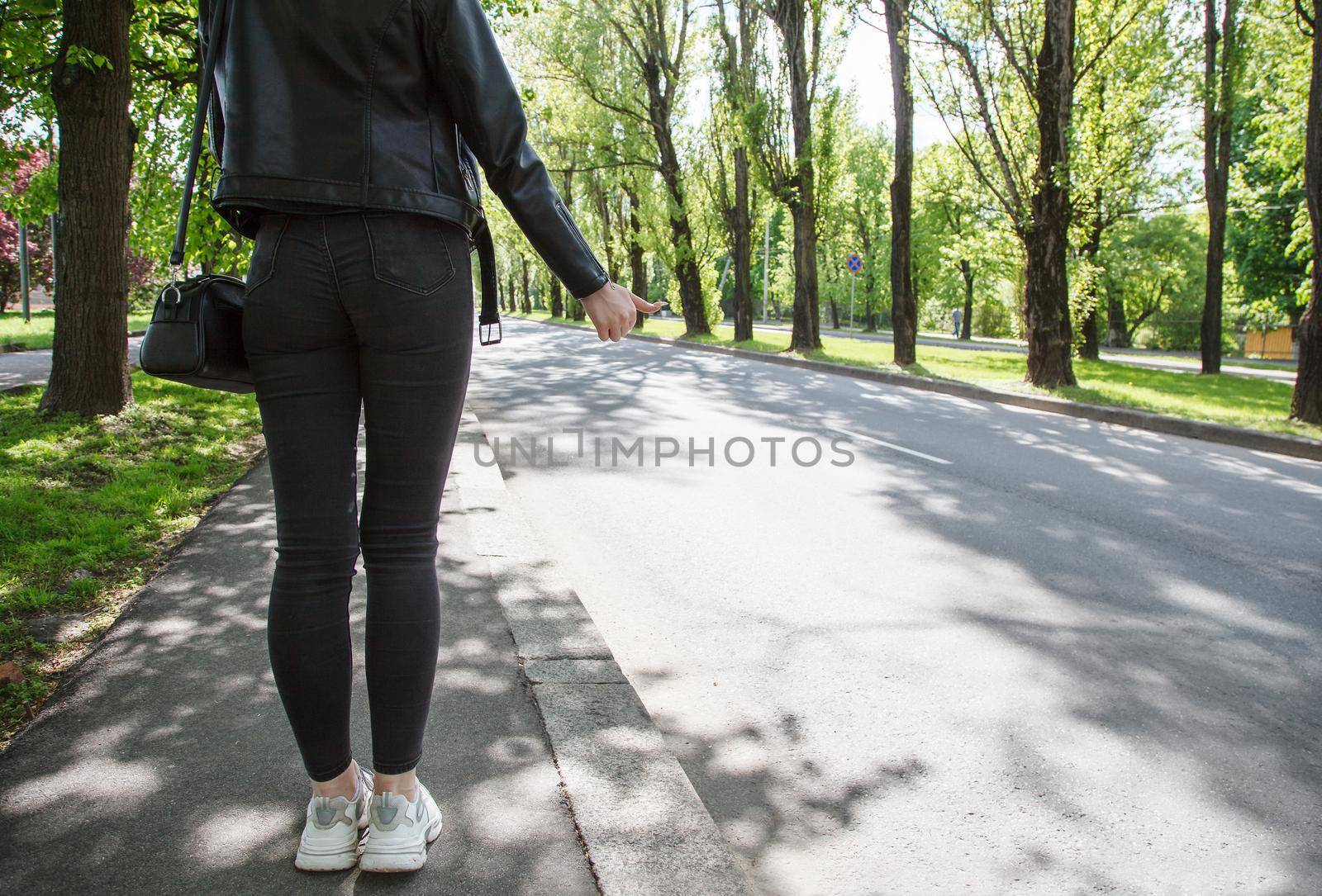 girl in black jacket and jeans stops the car on sunny day. back view