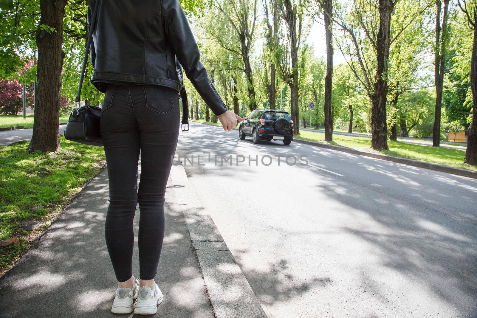 girl in black jacket and jeans stops the car on sunny day. back view
