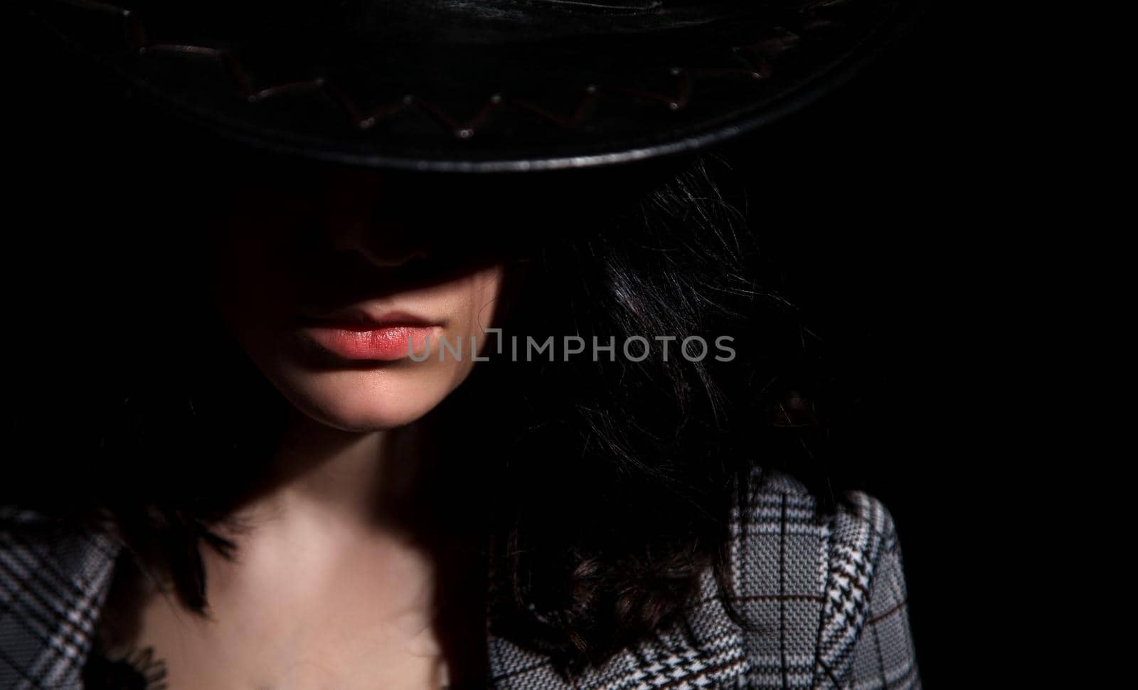 portrait of a young beautiful brunette girl in jacket and hat in studio on black background