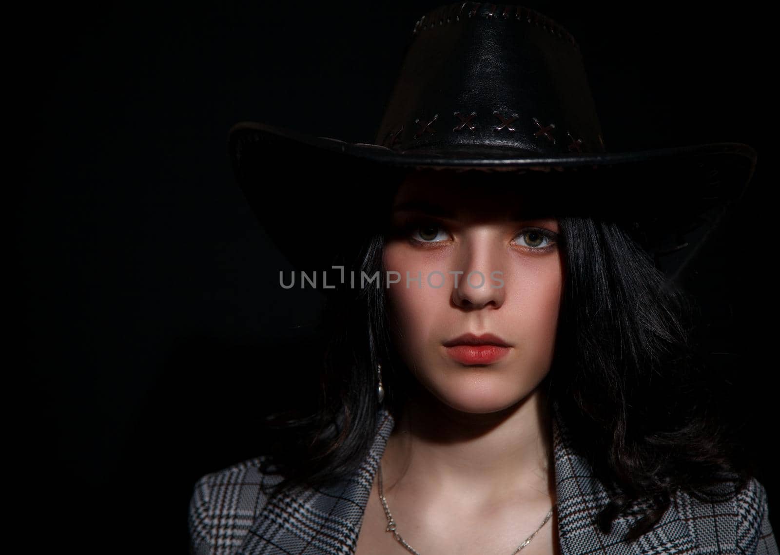 portrait of a young beautiful brunette girl in jacket and hat in studio on black background