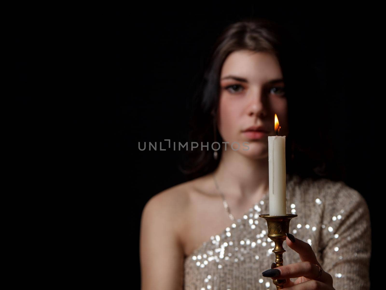 young beautiful brunette girl in bright dress holding burning candle in studio on black background