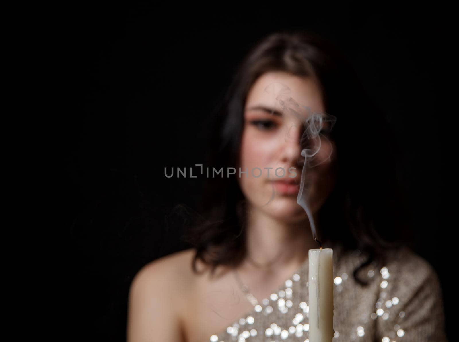 young beautiful brunette girl in bright dress holding candle in studio on black background