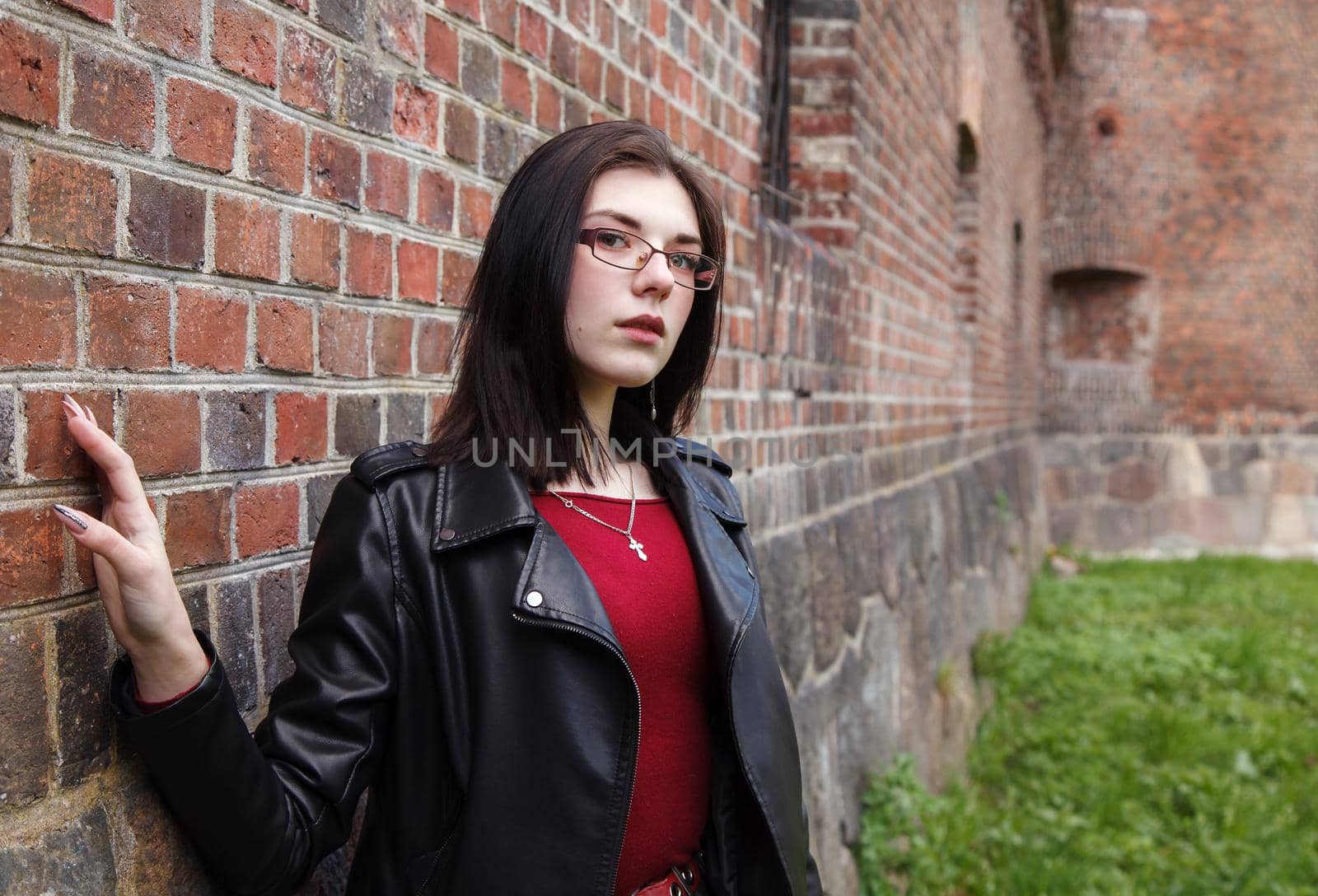 young beautiful girl in black jacket and jeans stands near the old fortress wall on sunny day. closeup outdoor