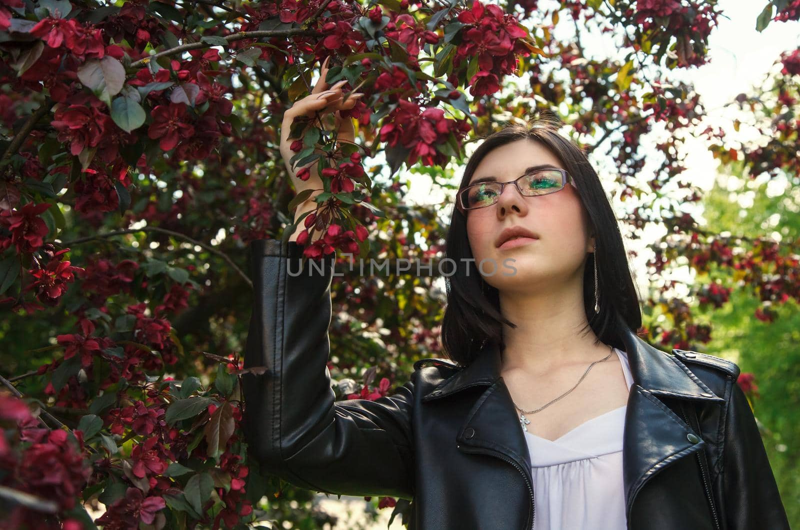 portrait of young beautiful brunette girl in black jacket standing near cherry blossoms on sunny spring day. outdoor closeup