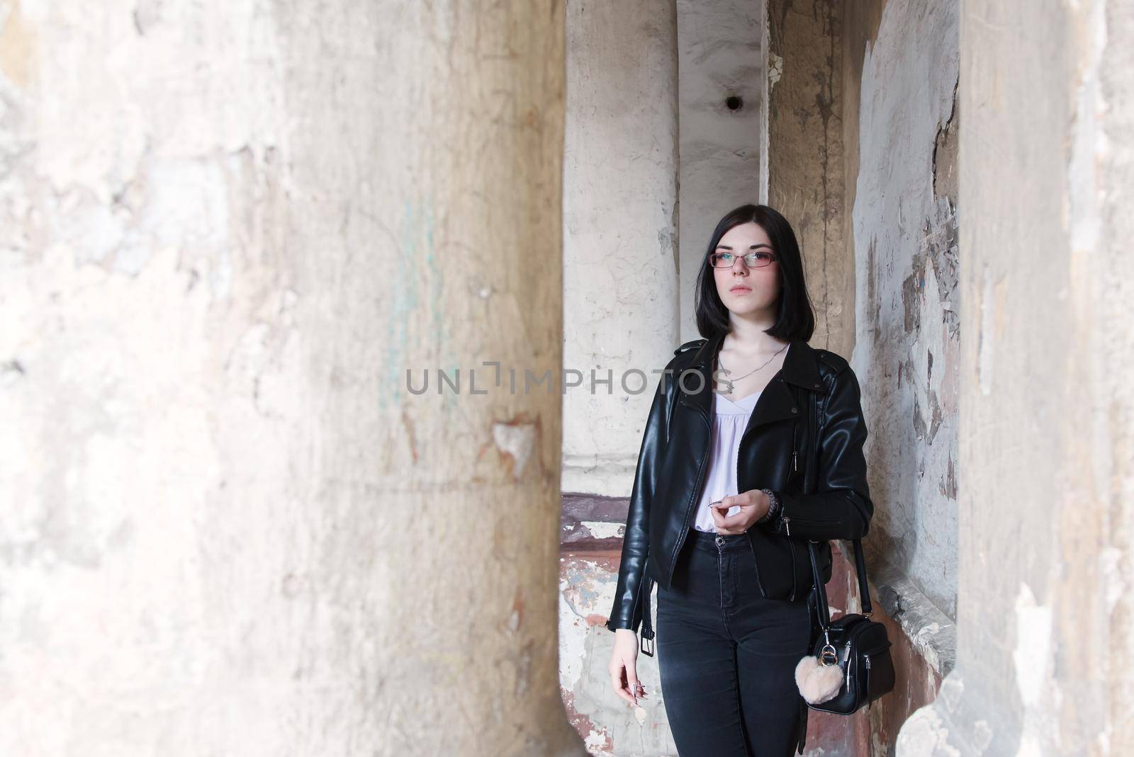 sad young girl in black jacket and jeans stands in old arch on city street on summer day. closeup outdoor