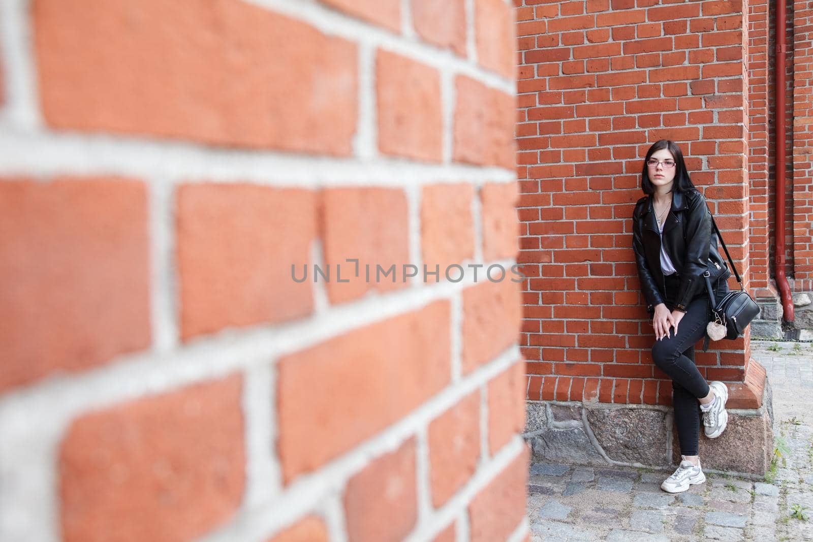 young beautiful brunette girl stands near wall of gothic church by raddnatt