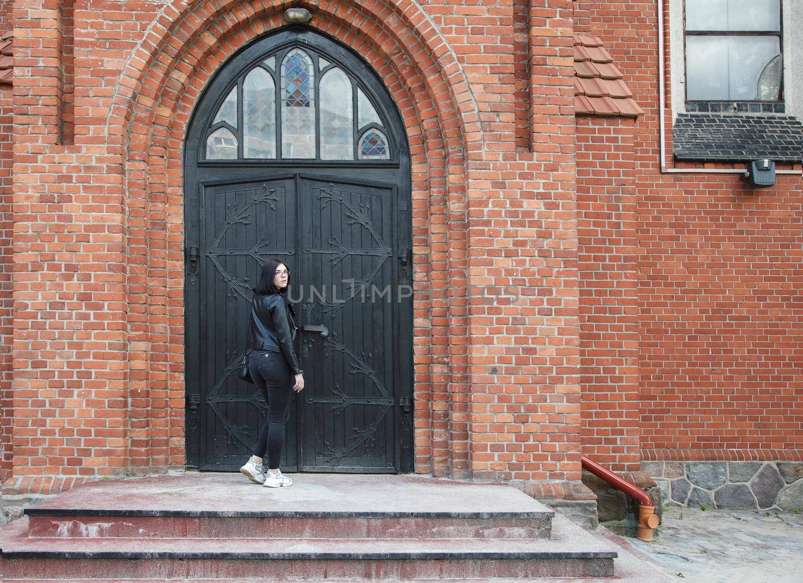 beautiful brunette girl stands near door of gothic church by raddnatt
