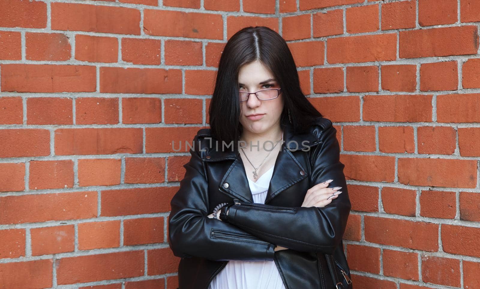 young beautiful brunette girl in black jacket and jeans stands near wall of gothic church on summer day. outdoor closeup