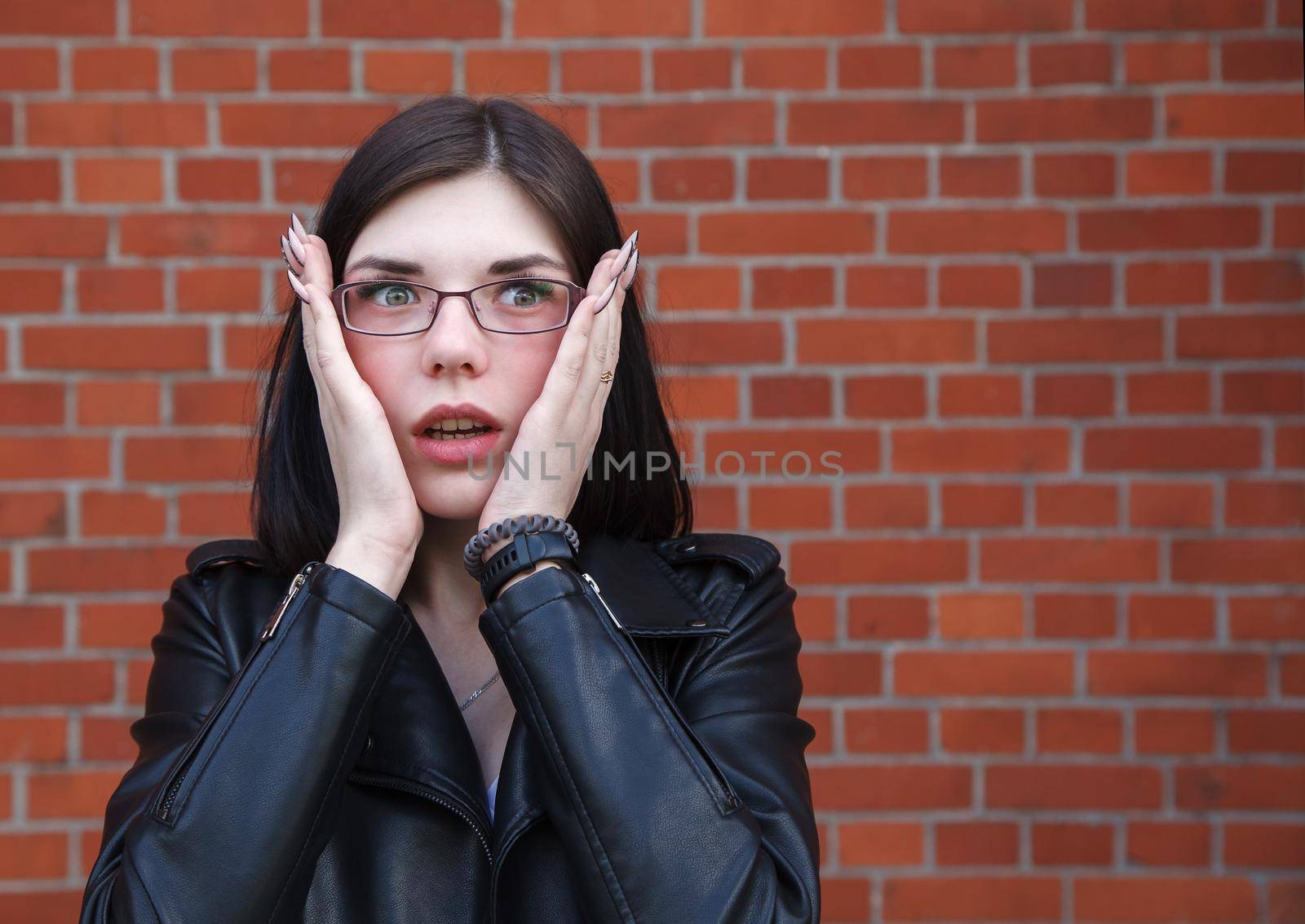 amazed young beautiful brunette girl in black jacket outdoor closeup on brick wall background