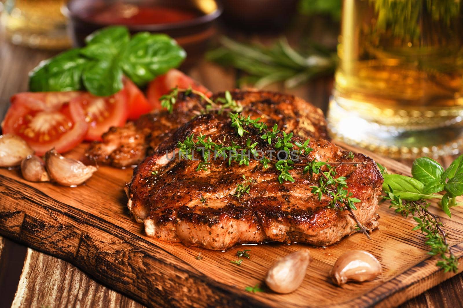 Fried pork steak on a wooden board to serve with vegetables and a mug of beer.
