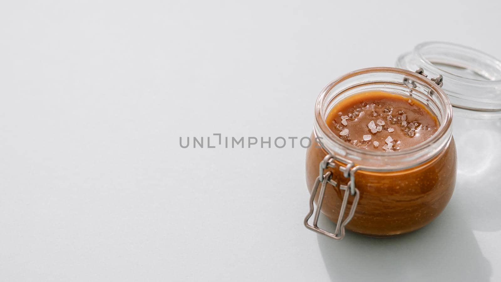Salted caramel in glass jars on light neutral background. Brown caramel or condensed milk with sea salt crystalls. Long horizontal banner, copy space left