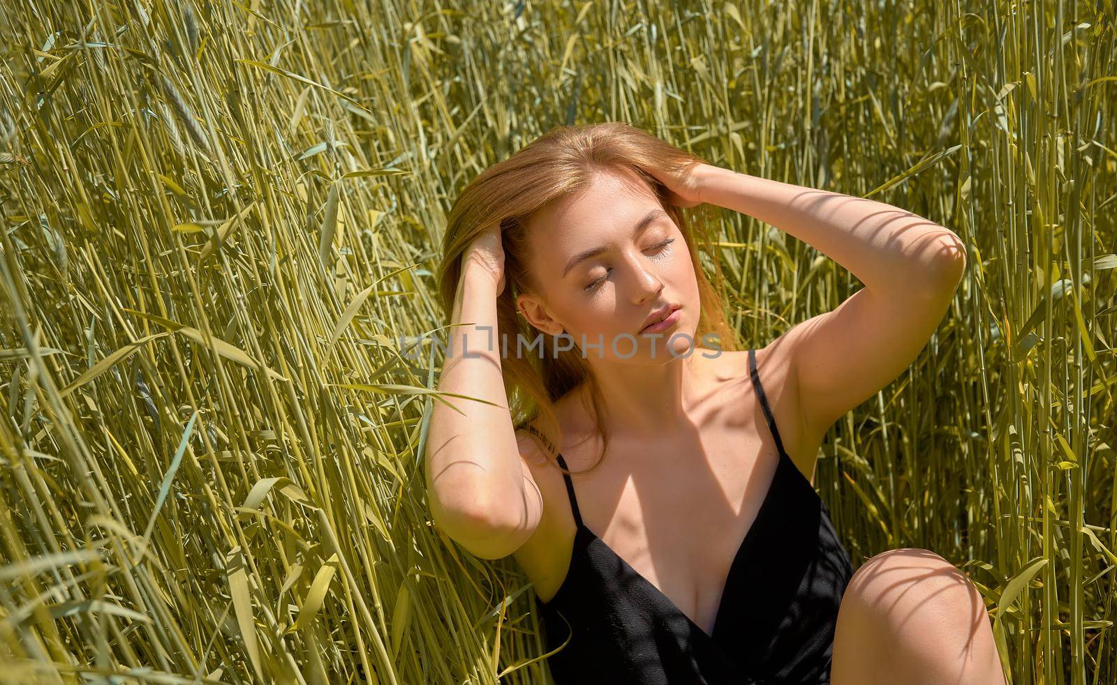 beautiful young woman sitting in the grass on the spring green field by AliaksandrFilimonau