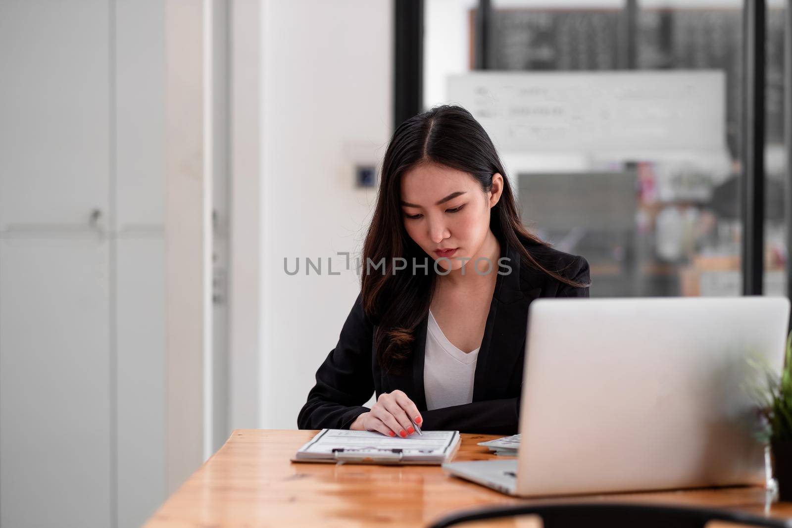 sian young woman seriously working on computer laptop and checking data report at home office.