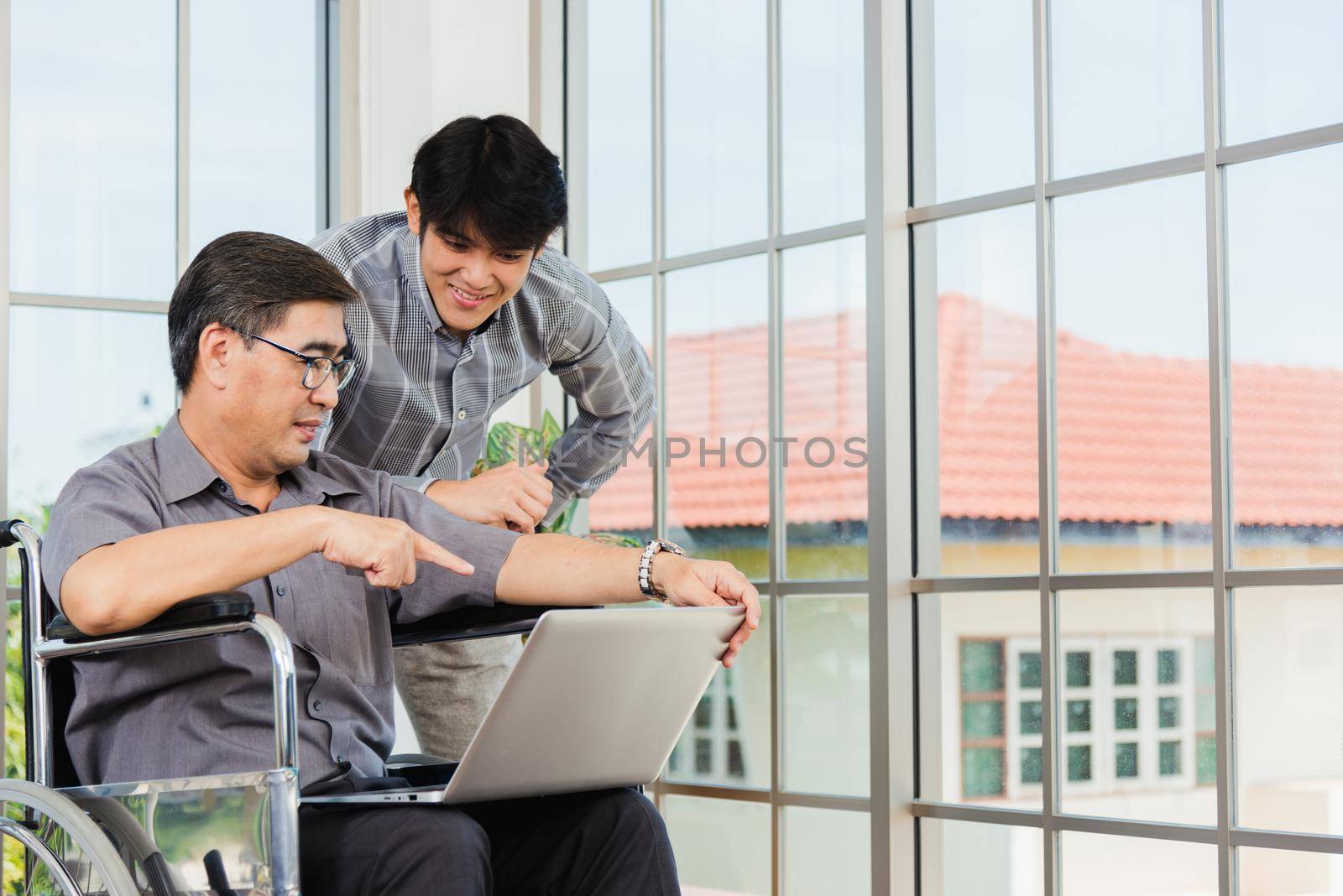 Asian senior disabled businessman in a wheelchair with laptop computer discuss together with team in office. Old father man sitting wheelchair and his son talking video calls conference on laptop