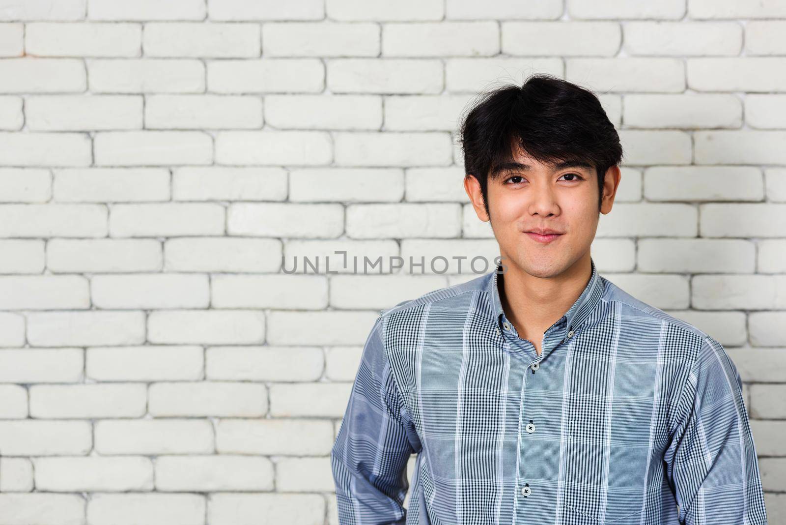 Portrait of Asian handsome young man he smile and looking at camera on brick wall background. Happy guy smiling. Portrait of laughing young man standing with confident