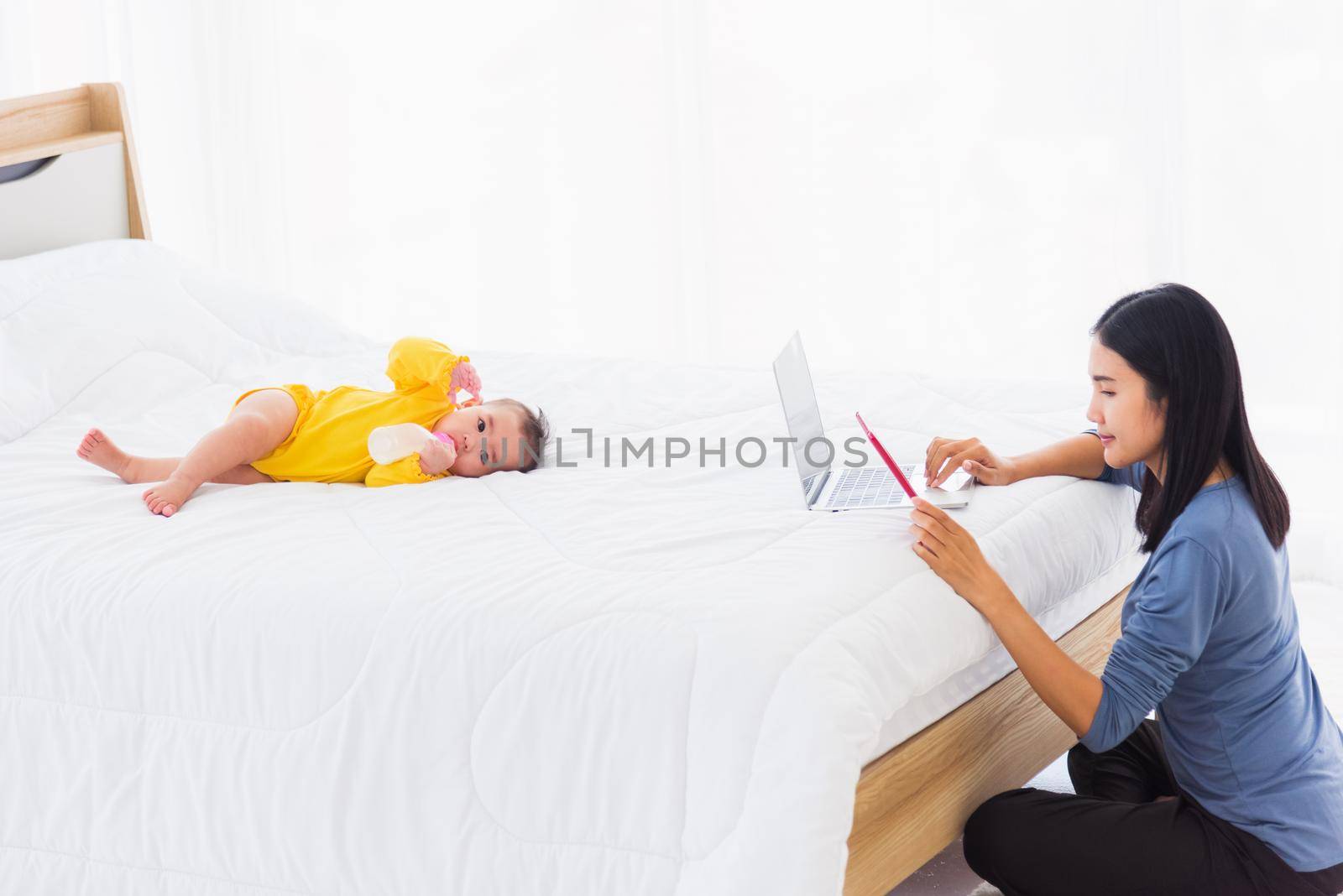 woman is working busy on laptop computer and tablet at home while her  baby is sleeping by Sorapop