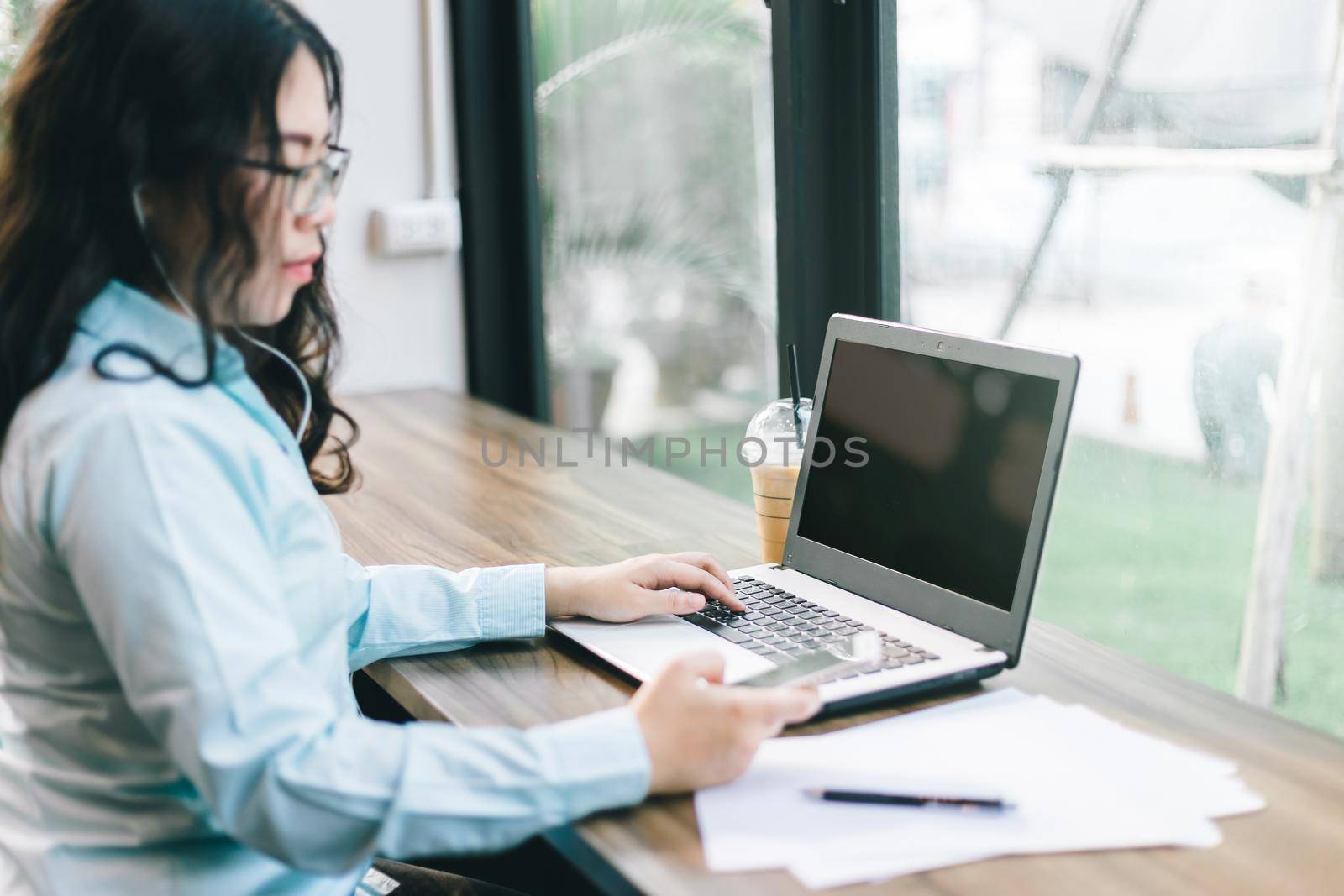 Business Asian woman be dressed in earphone working with smartphone focus of laptop computer on in coffee shop like the background.  by tinapob2534