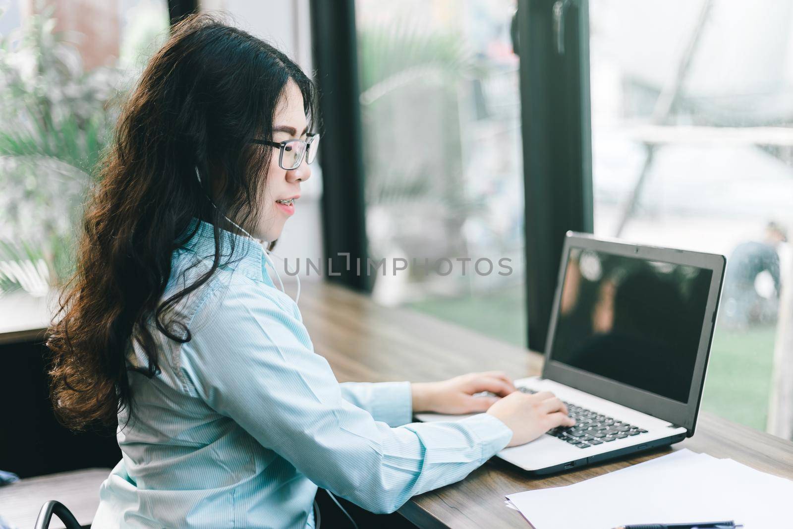 Business Asian woman be dressed in earphone working with smartphone and laptop computer on in coffee shop like the background. 