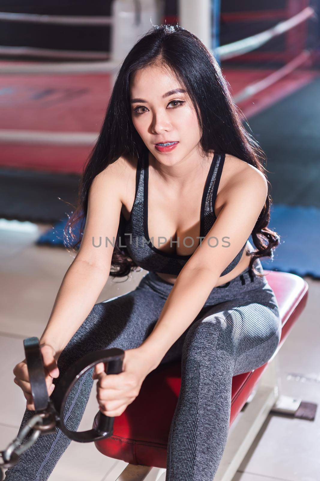 Fitness Asian women performing doing exercises training with rowing machine (Seat Cable Rows Machine) in sport gym interior and fitness health club with sports exercise equipment Gym background. by tinapob2534