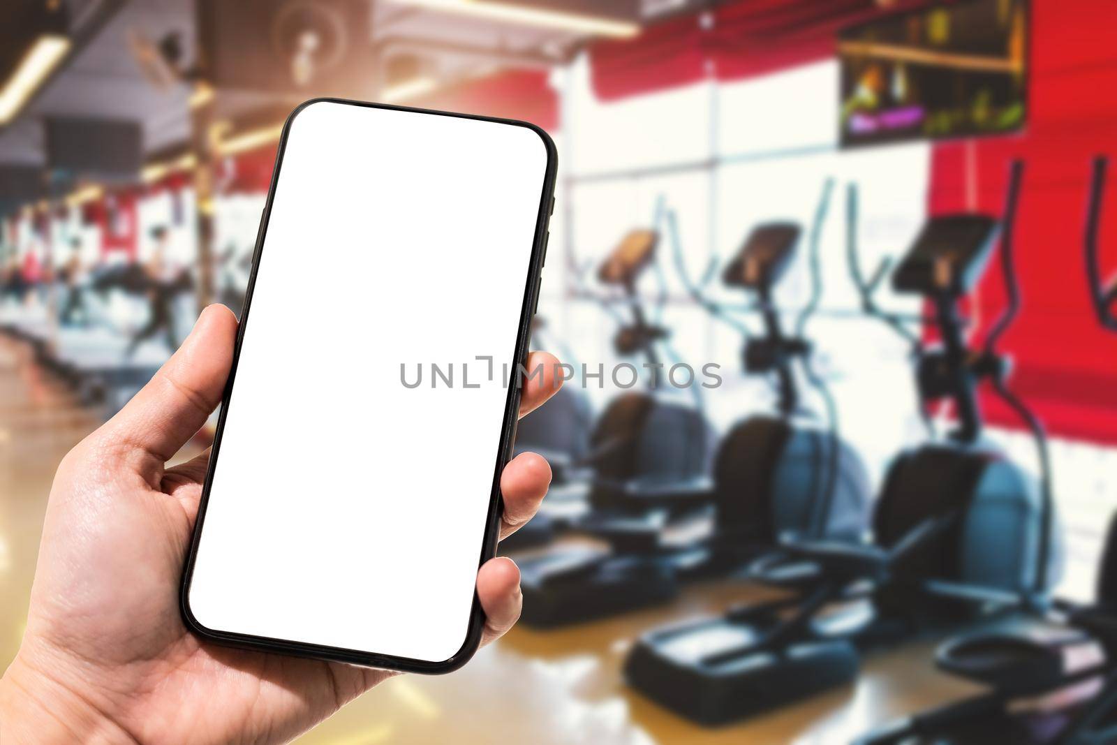 Close-up of female use Hand holding smartphone blurred images touch of Abstract blur of defocused sport gym interior and fitness health club with sports exercise equipment Gym blur background.